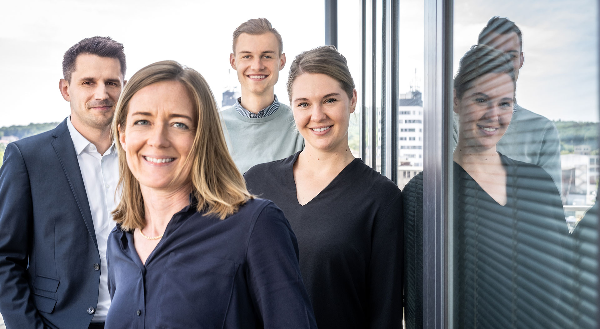 bjb-ueber-uns-mitarbeiter-zwei-frauen-im-vordergrund-zwei-maenner-im-hintergrund-spiegelung-im-fenster